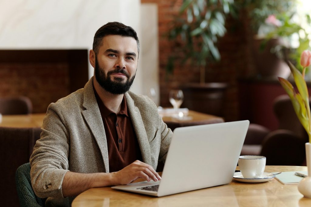 smiling restaurant owner using a laptop, with a cup of coffee next to it