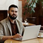 smiling restaurant owner using a laptop, with a cup of coffee next to it