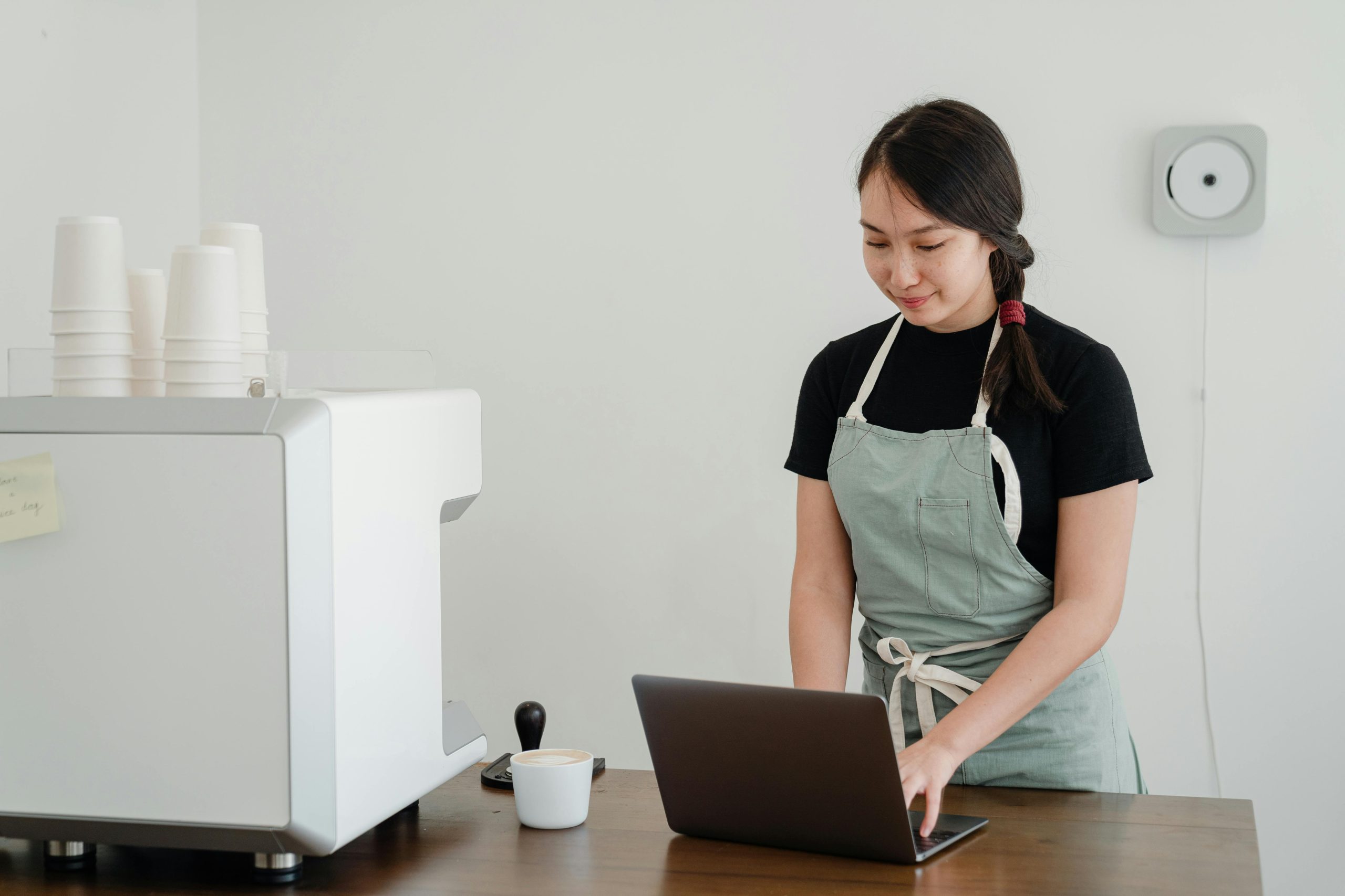 coffee shop owner typing on a laptop, next to a commercial coffee maker